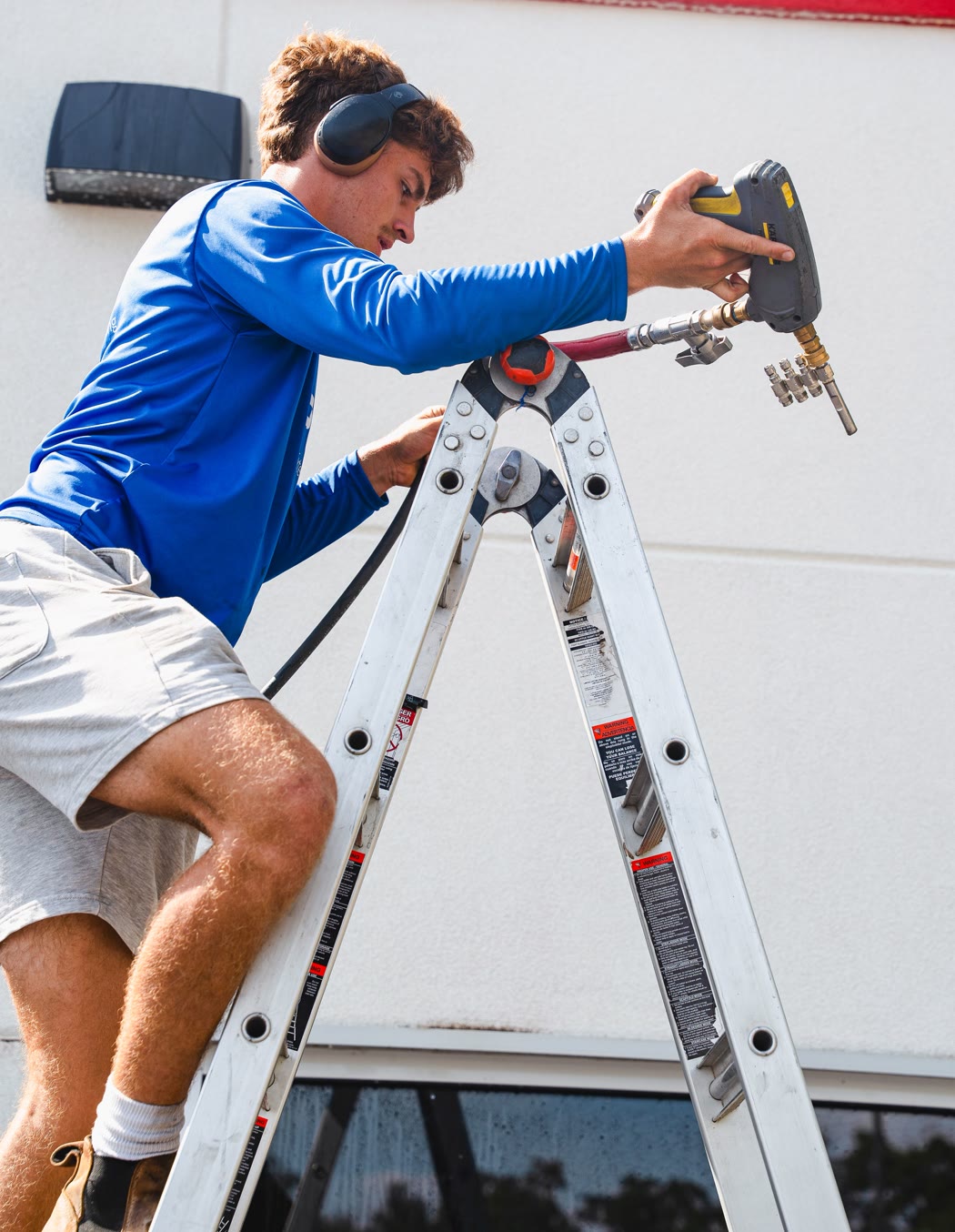 Peak technician washing the upper wall of a commercial building from a ladder
